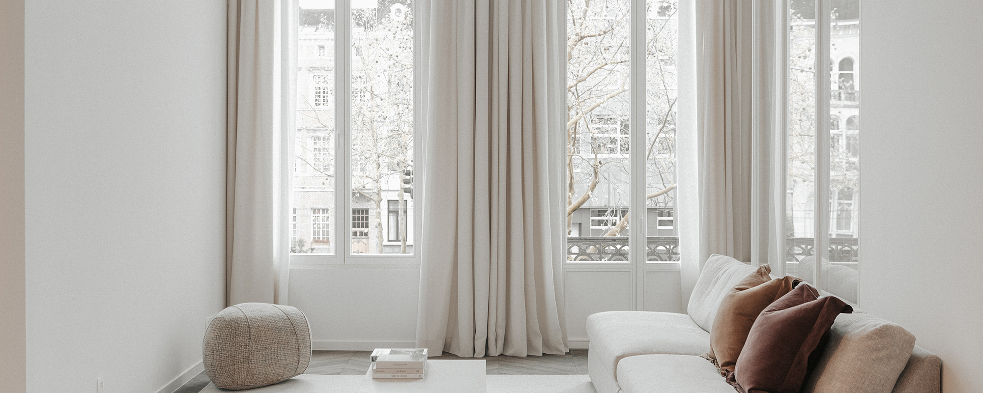 Linen Drapery, Verellen: Floor-to-ceiling neutral Bozeman draperies flow elegantly across tall windows, softly diffusing natural light in a calm, modern living room.