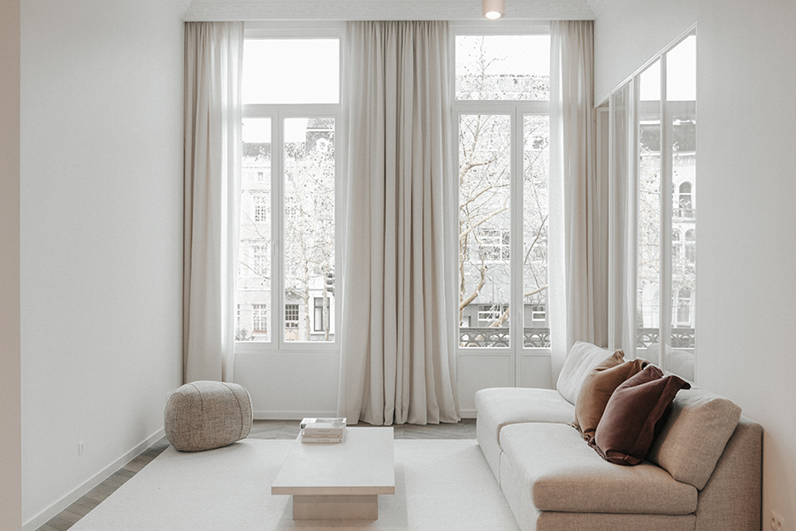 Linen Drapery, Verellen: Floor-to-ceiling neutral Bozeman draperies flow elegantly across tall windows, softly diffusing natural light in a calm, modern living room.