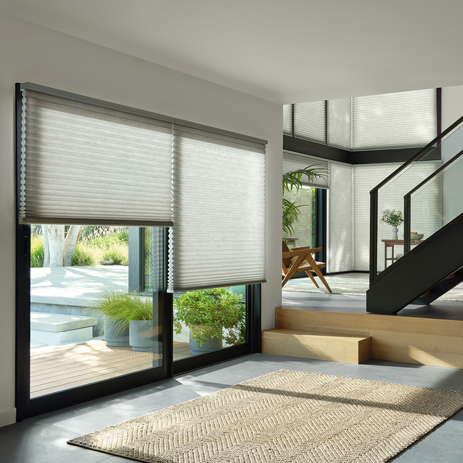 Duette honeycomb shades on tall windows in a double-height hallway with stone walls, demonstrating energy-efficient shades that Bozeman homeowners love.