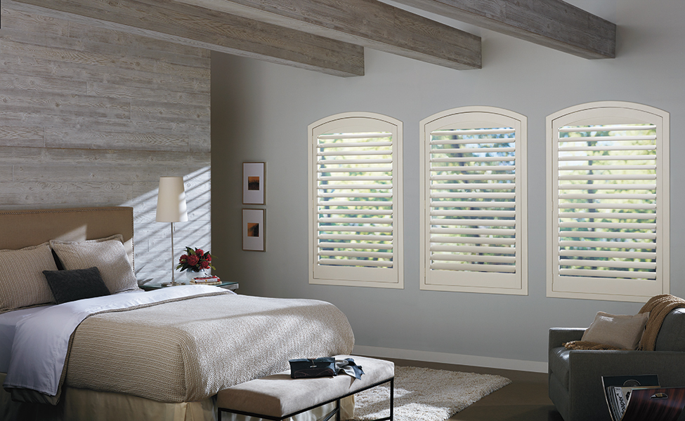 Bright white NewStyle® Hybrid Bozeman shutters, which add clean lines and soft natural light to a cozy, modern bedroom with exposed wood beams.