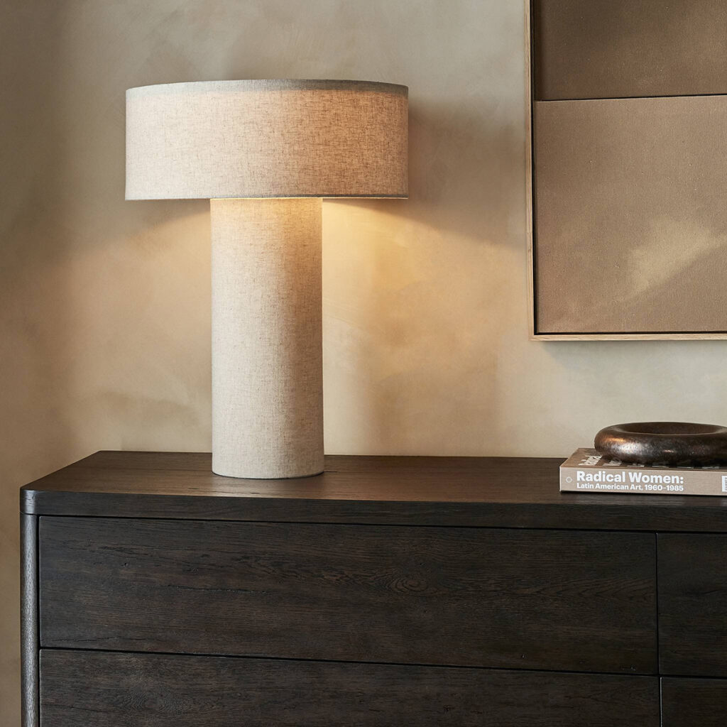 Tall cream cylindrical table lamp with a textured base and natural linen shade on a dark wood console.