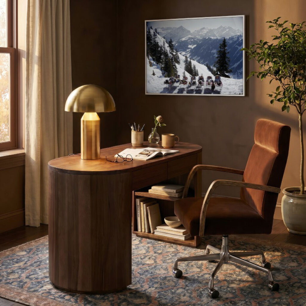 Brass dome table lamp on a curved wood desk in a warm home office.