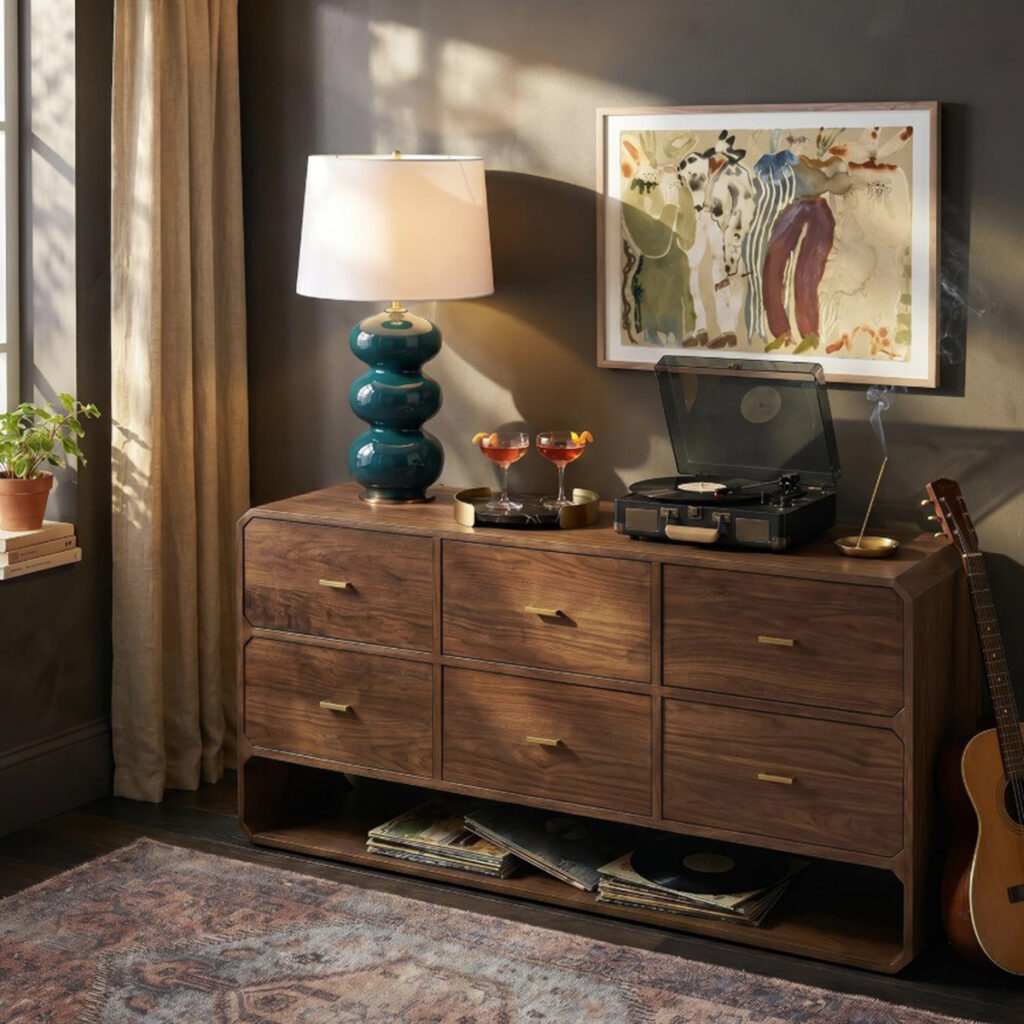 Teal stacked ceramic table lamp with a white shade on a wood dresser beside a record player.