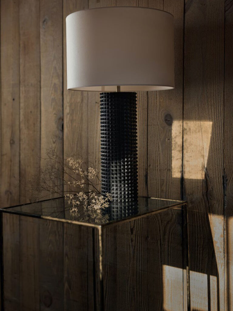 Black textured column table lamp with a white drum shade on a glass side table.