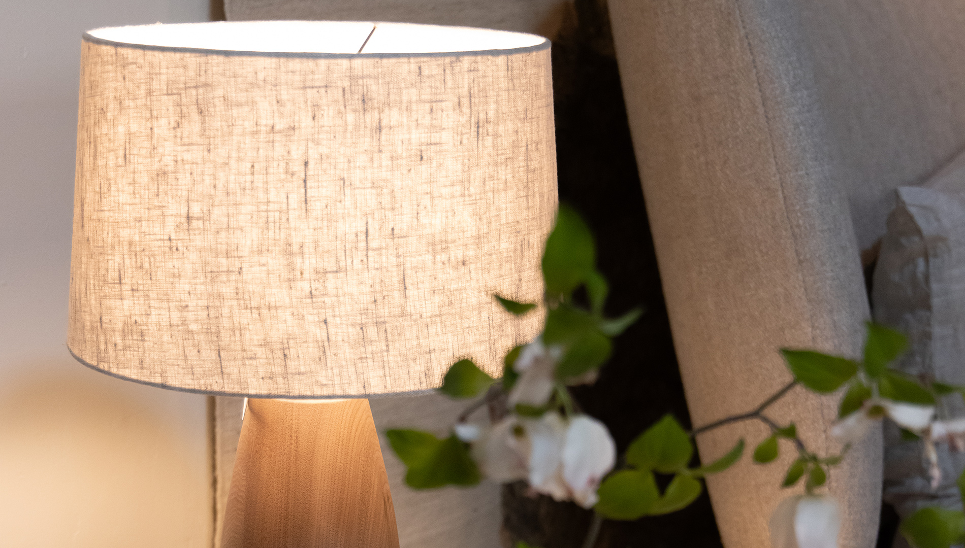 Wood table lamp with a linen shade on a side table accented with books and flowering branches.