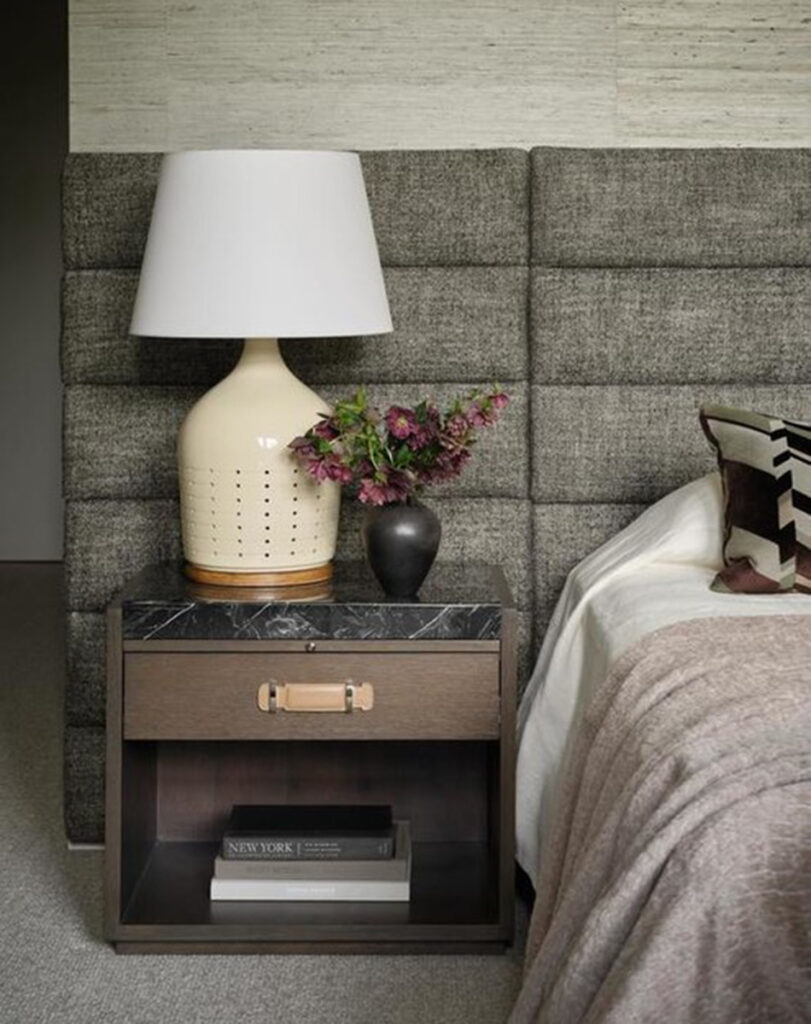 Cream ceramic bedside table lamp with a white shade on a marble-top nightstand.