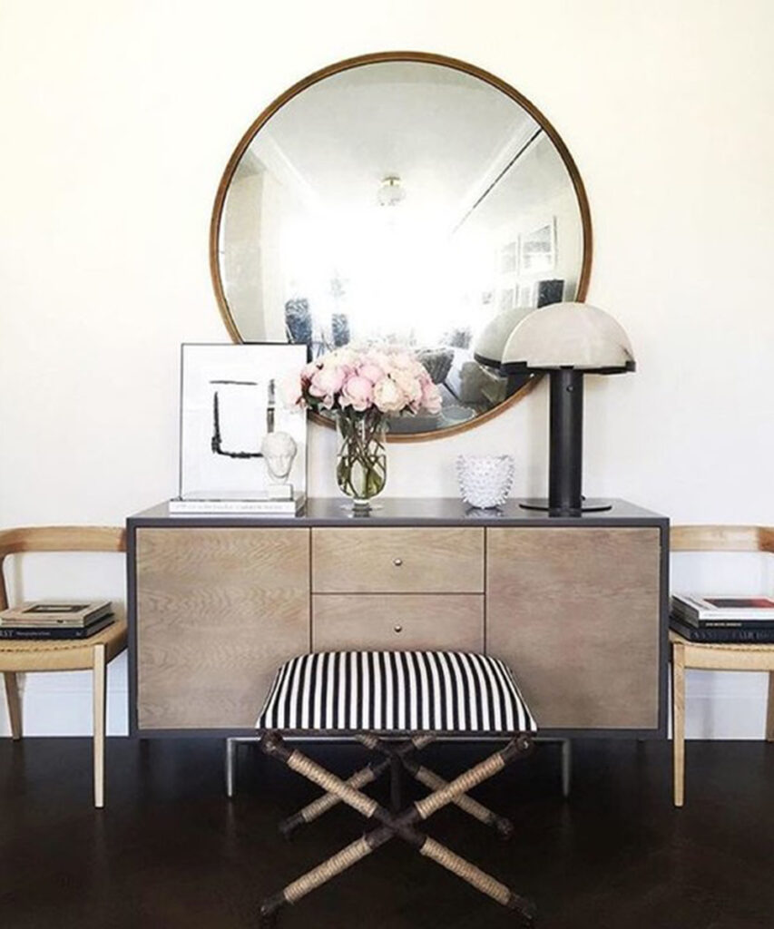 Black table lamp with a rounded dome shade on a console beneath a large round mirror.