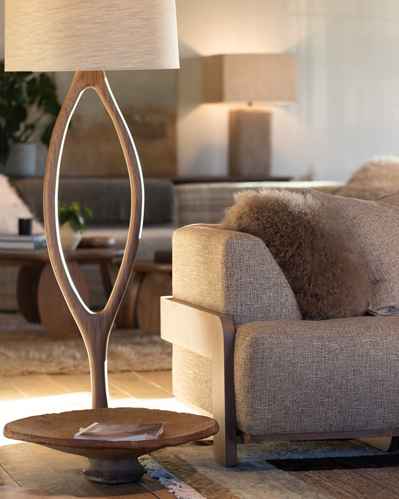 A Verellen “Urbino” floor lamp. This Sculptural floor lamp with an open oval frame and white drum shade stands beside a neutral upholstered chair.